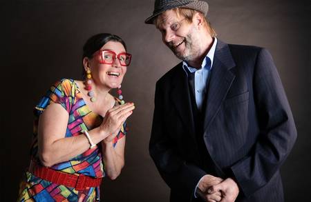 Zwei Personen, eine in buntem Kleid, die andere im Anzug mit Hut.